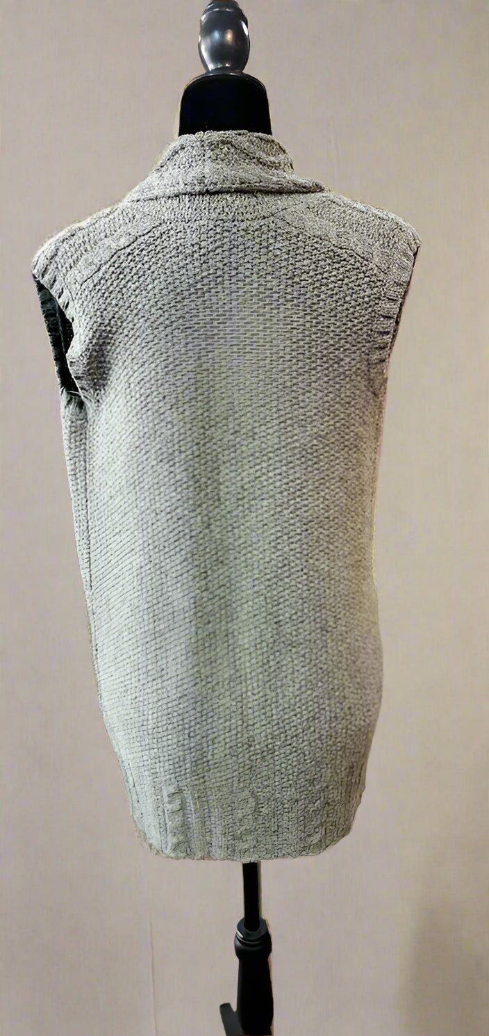 Green knitted vest on a mannequin in a store setting with racks of clothes in the background.